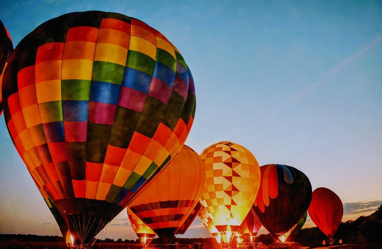 Hot air balloons, brightly colored and inflated, against a dusky blue sky at dusk.