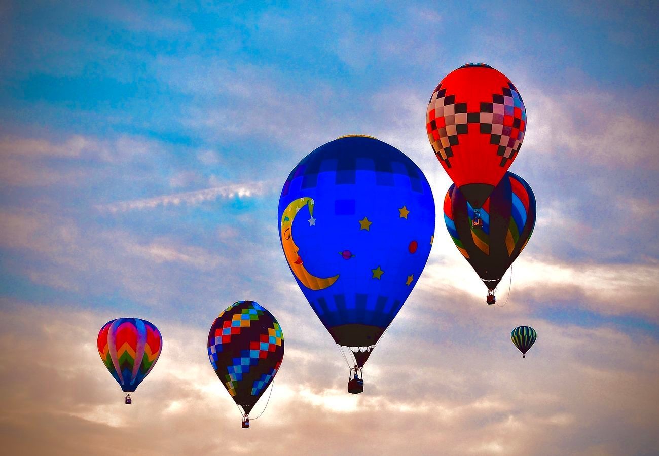 Hot air balloons of various colors floating in a cloudy sky.