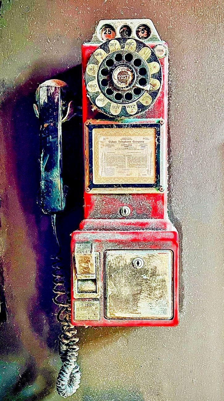 Red, weathered payphone mounted on a wall. Rotary dial, handset on the side, coin slot.