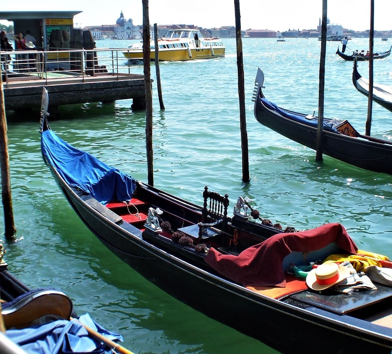 Gondolas docked in the turquoise waters of Venice, Italy. A blue tarp and red blanket rest in one.