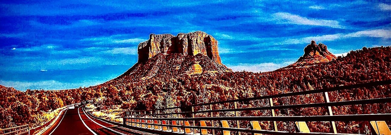 Landscape with a road leading towards a large rock formation under a blue sky.