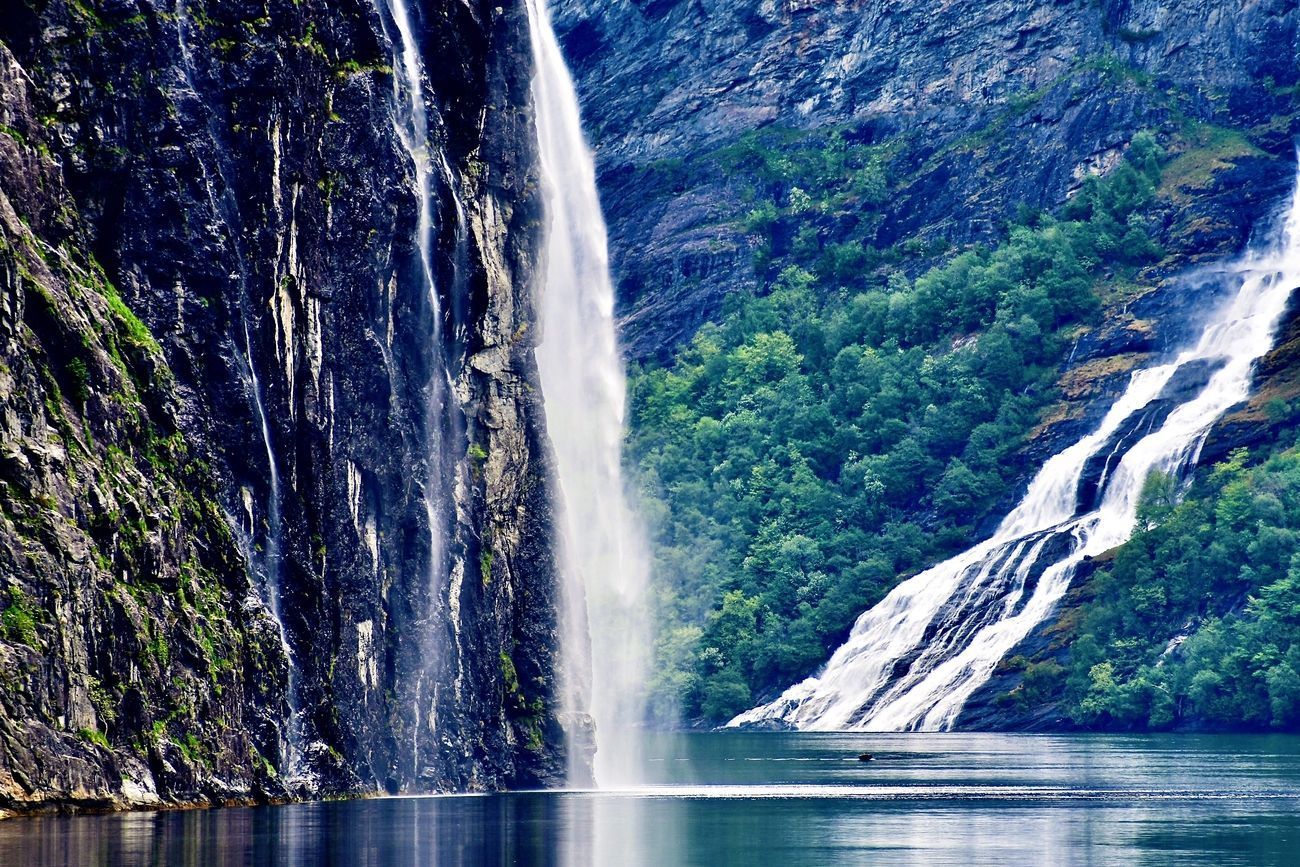 Waterfall cascading down a dark, rocky cliff into a body of water, with lush green foliage.