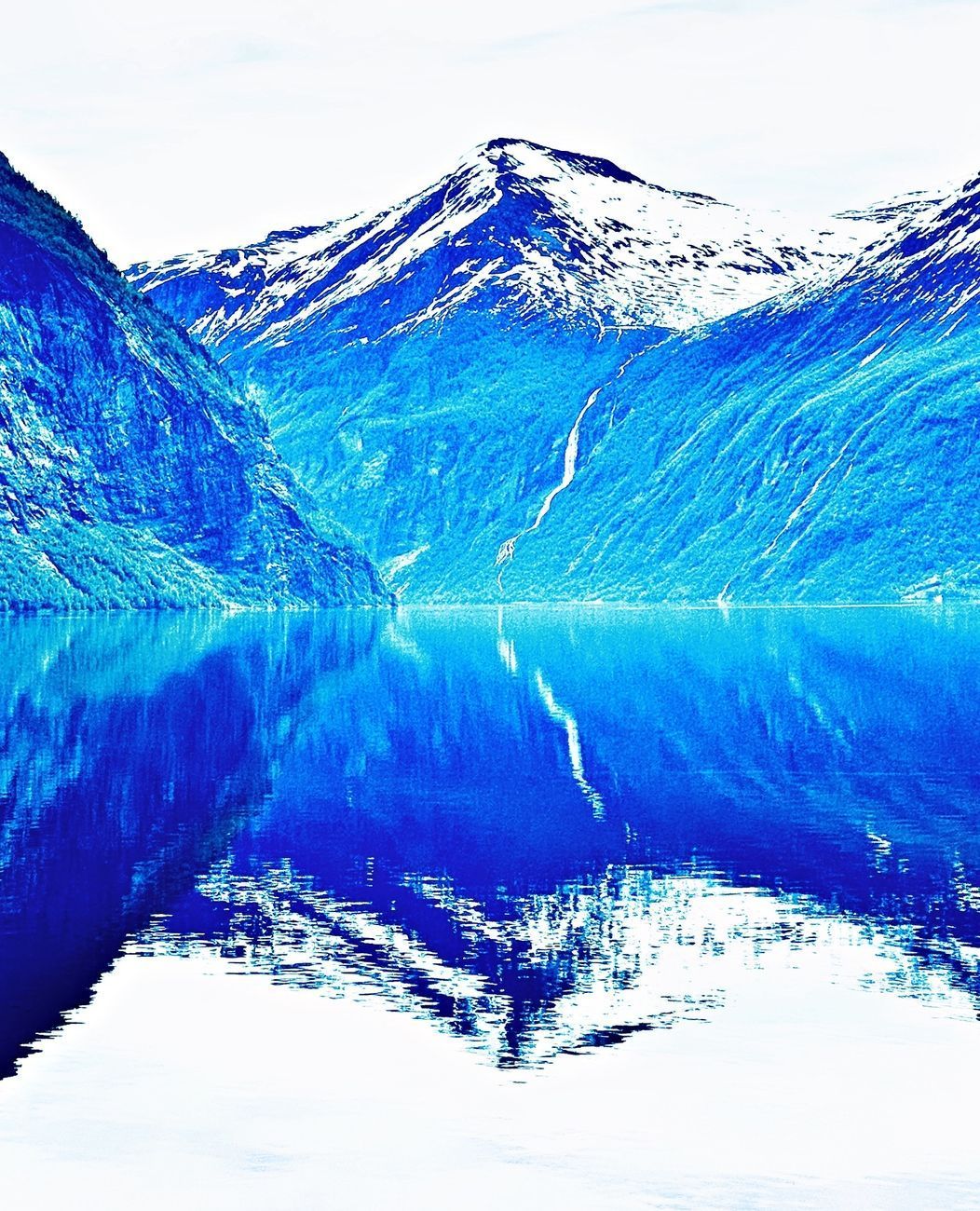 Blue mountains reflected in tranquil water; snow-capped peak.