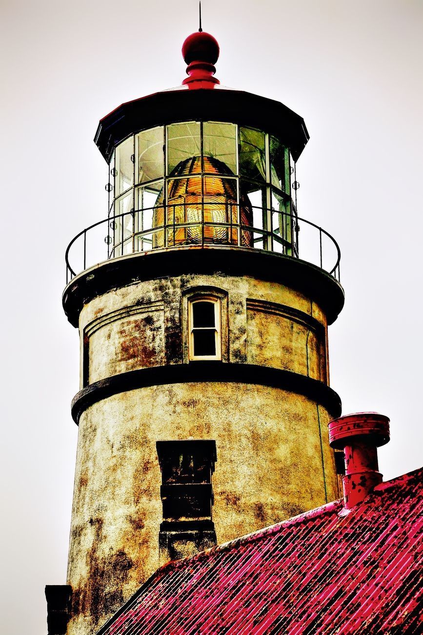 Lighthouse with a red roof. The tower is tan and weathered, with a glass-enclosed lantern room at the top.