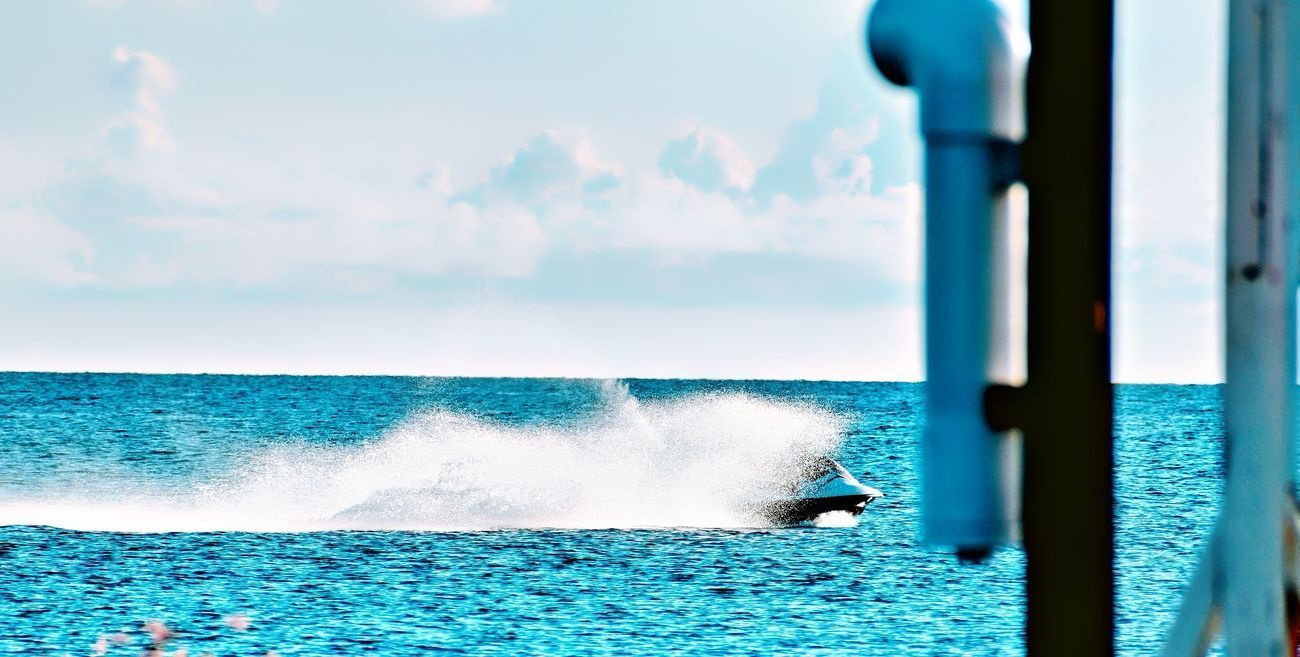 Jet ski speeding across blue ocean, creating a large spray.