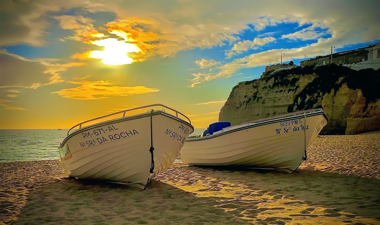 Two white boats on a sandy beach at sunset, with a cliff in the background.