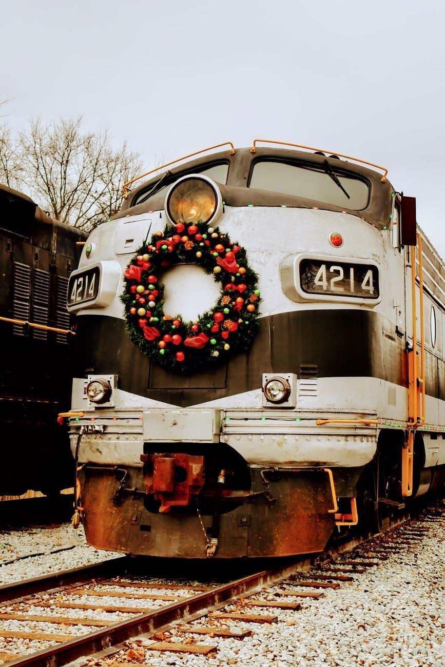 A vintage train engine with a Christmas wreath on its front, parked on tracks.