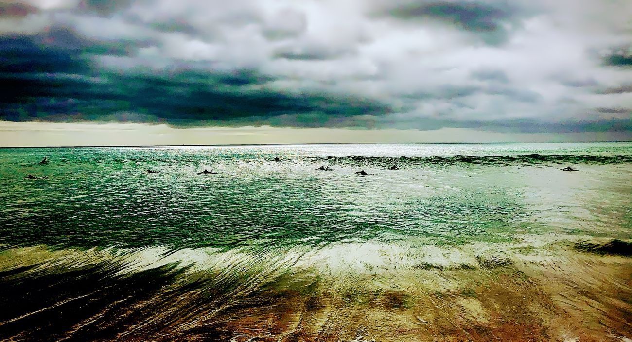 Overcast sky over ocean; waves crashing on beach. Dark clouds, teal water, sandy shore.