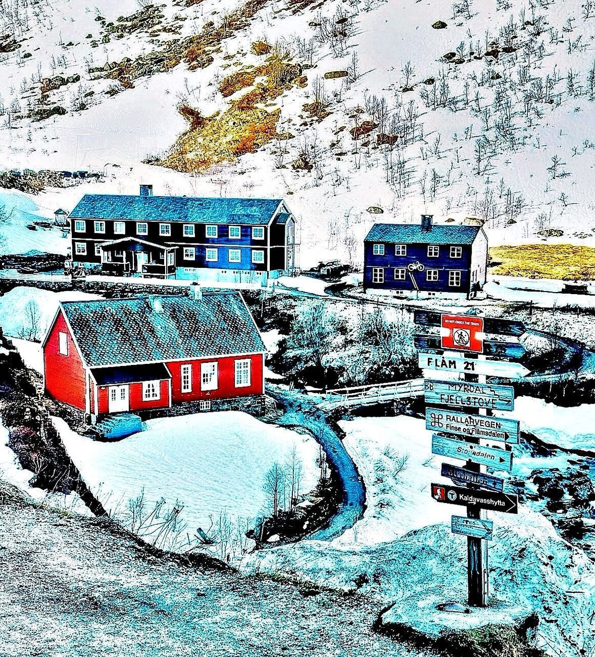 Snow-covered landscape with red and blue buildings. Signpost with directions.