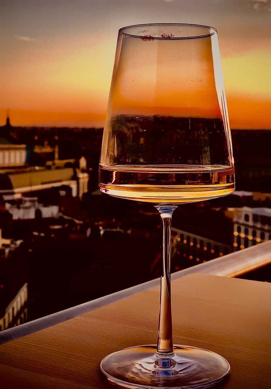 Wine glass filled with liquid, against a sunset cityscape.