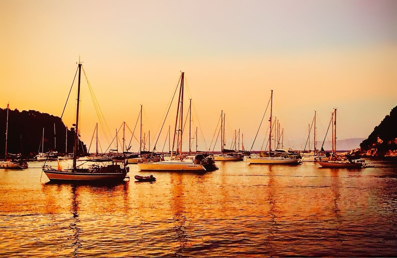 Sailboats docked in a harbor at sunset; golden light reflects on the water.