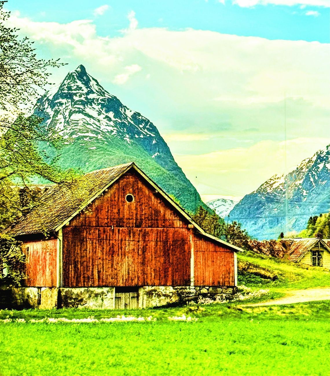 Red barn in a green field with snow-capped mountains in the background under a blue sky.