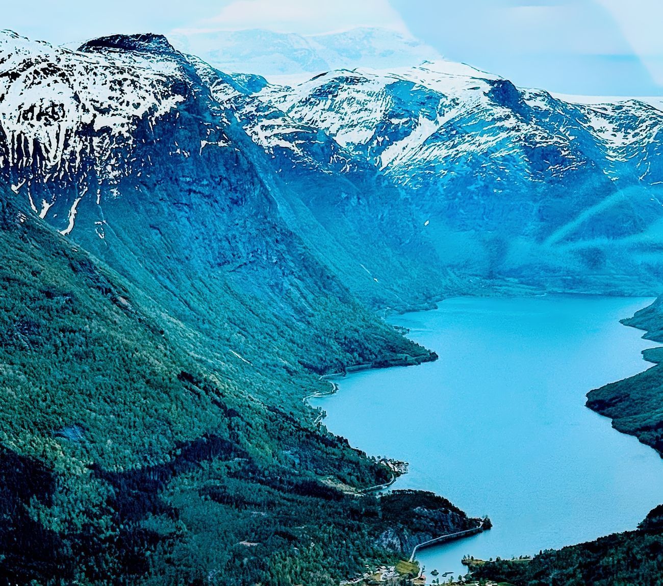 Blue lake surrounded by green mountains and snow-capped peaks in Norway.