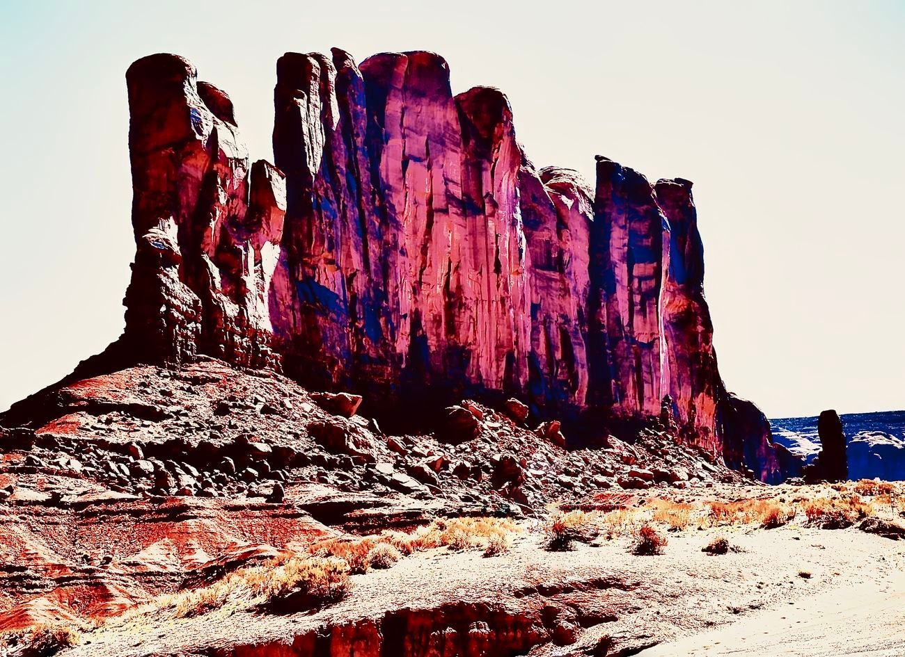 Red and brown rock formations in arid landscape with blue sky.
