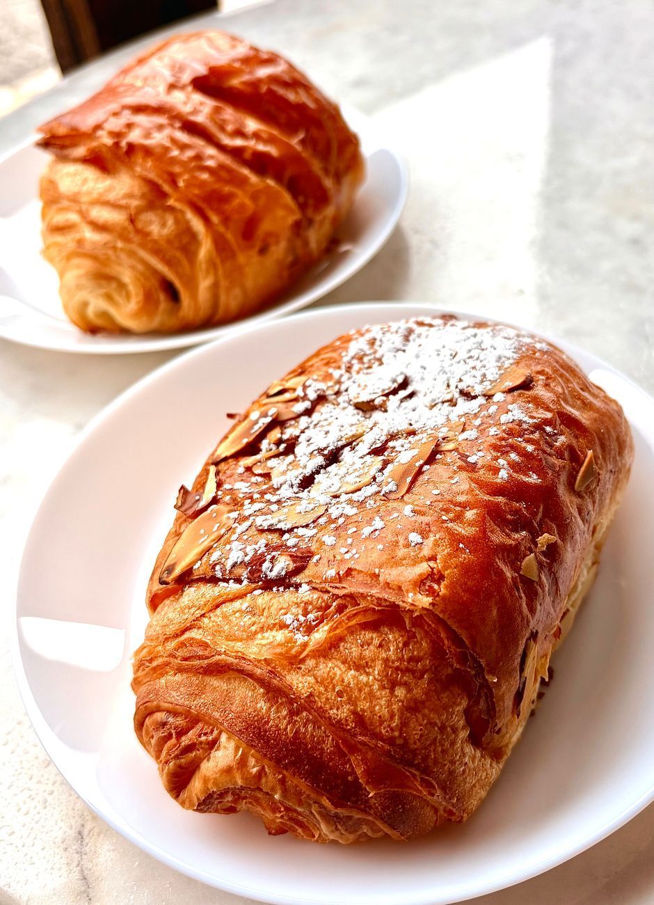 Two pastries on white plates. One croissant, one almond croissant with powdered sugar.