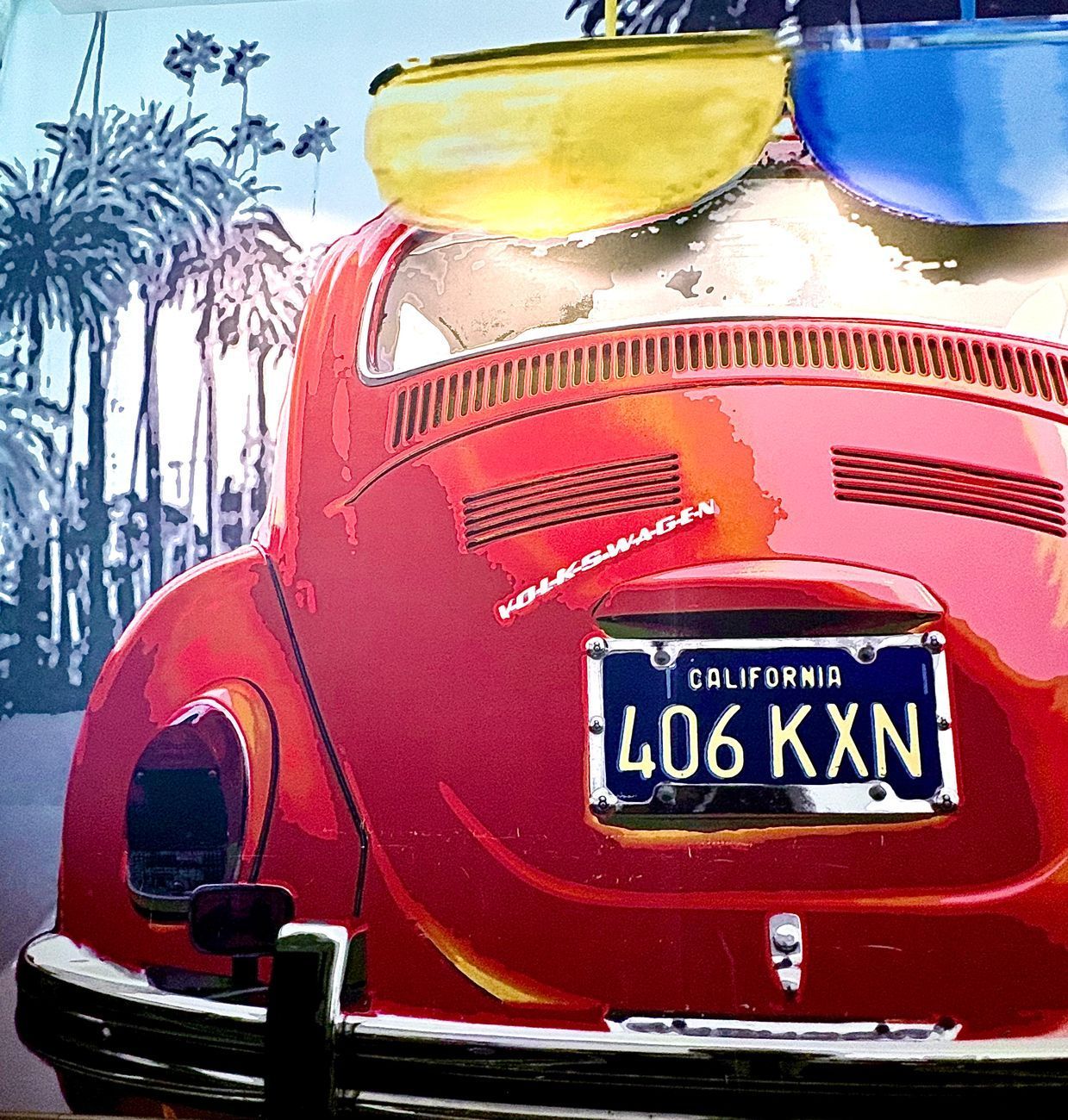 Red VW Beetle with California license plate, parked in front of palm trees.
