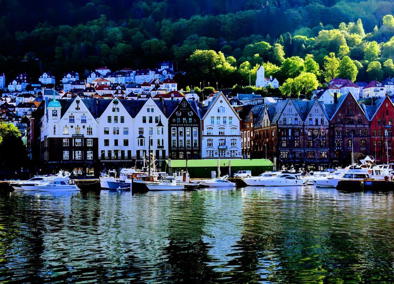 Waterfront view of colorful wooden buildings, boats, and green hillside in Bergen, Norway.