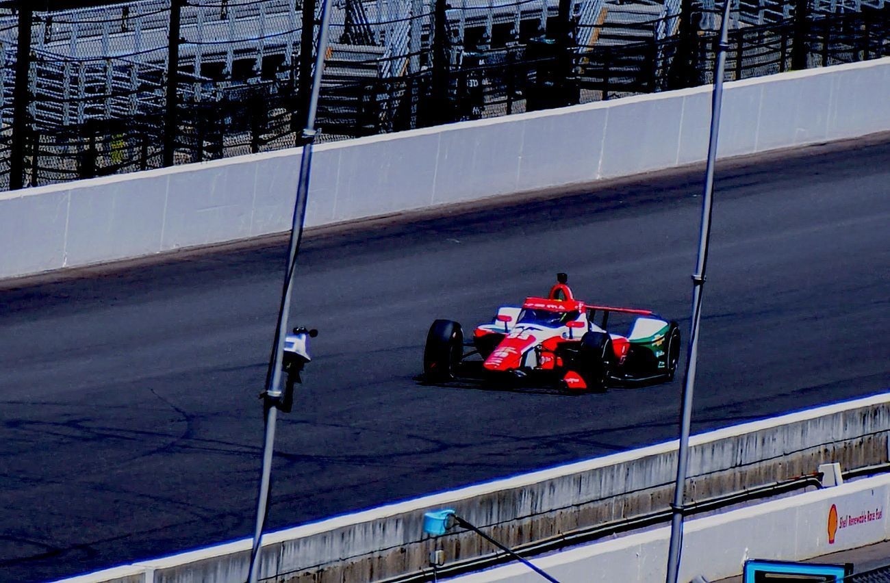 Race car speeds around a track, red and white with sponsor logos.