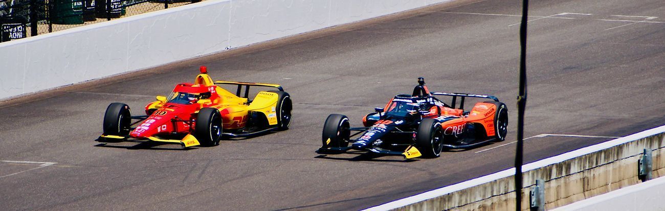 Two race cars, red and blue, racing side by side on a track.