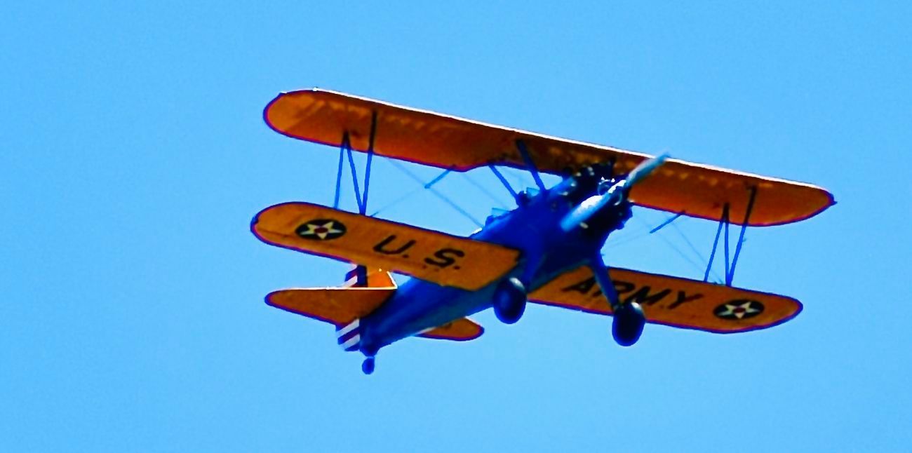 A blue and yellow biplane flying in a clear blue sky.