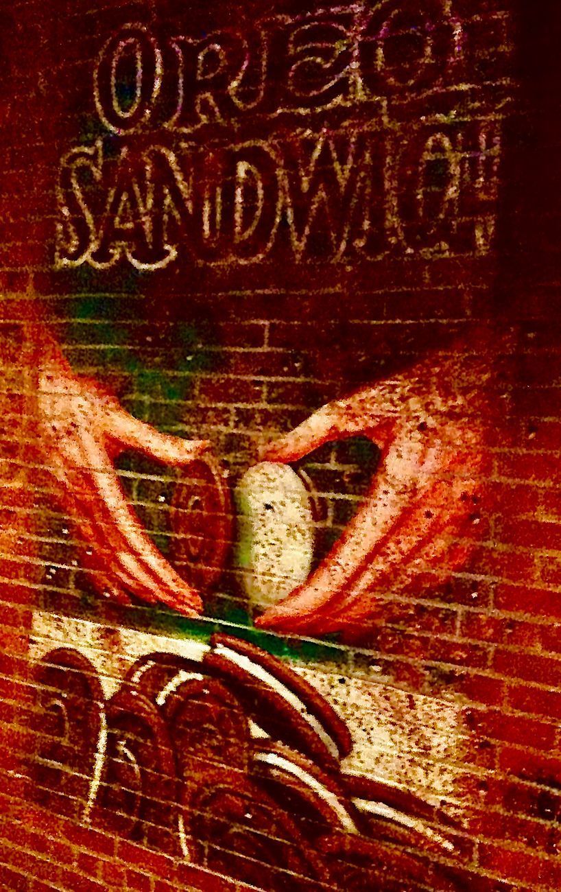 Mural on brick wall shows hands assembling an Oreo sandwich. Text above reads
