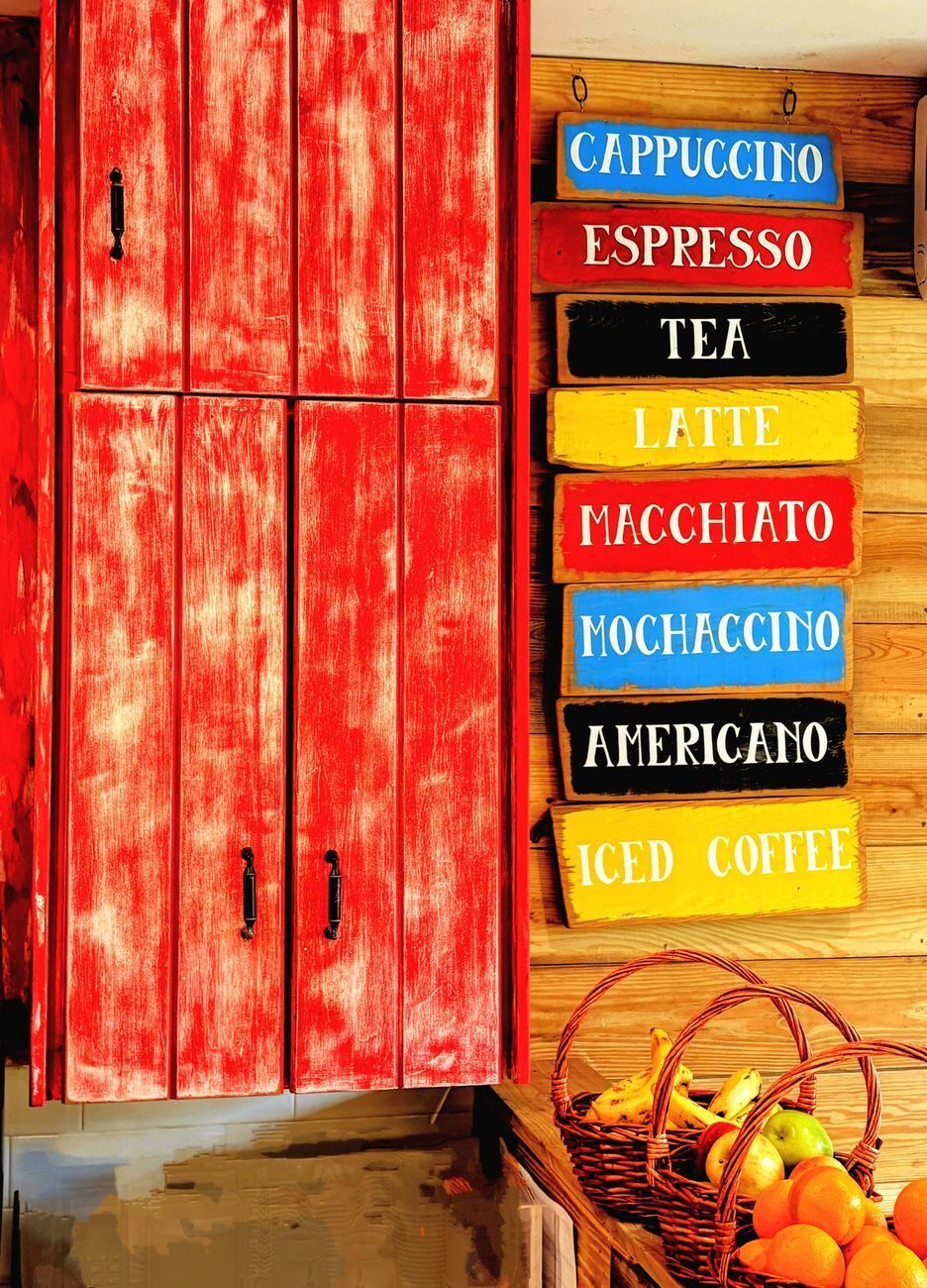 Red cabinet next to a wooden wall with colorful coffee signs and fruit baskets.