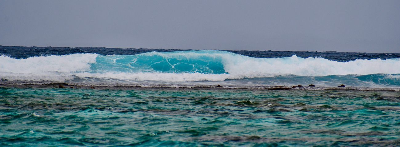 Ocean waves breaking over a reef, turquoise water with a gray sky.