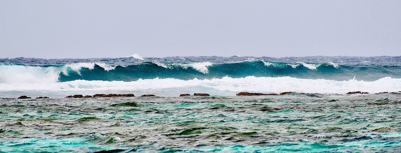 Waves crashing over a reef in shades of blue and white, with a gray sky overhead.