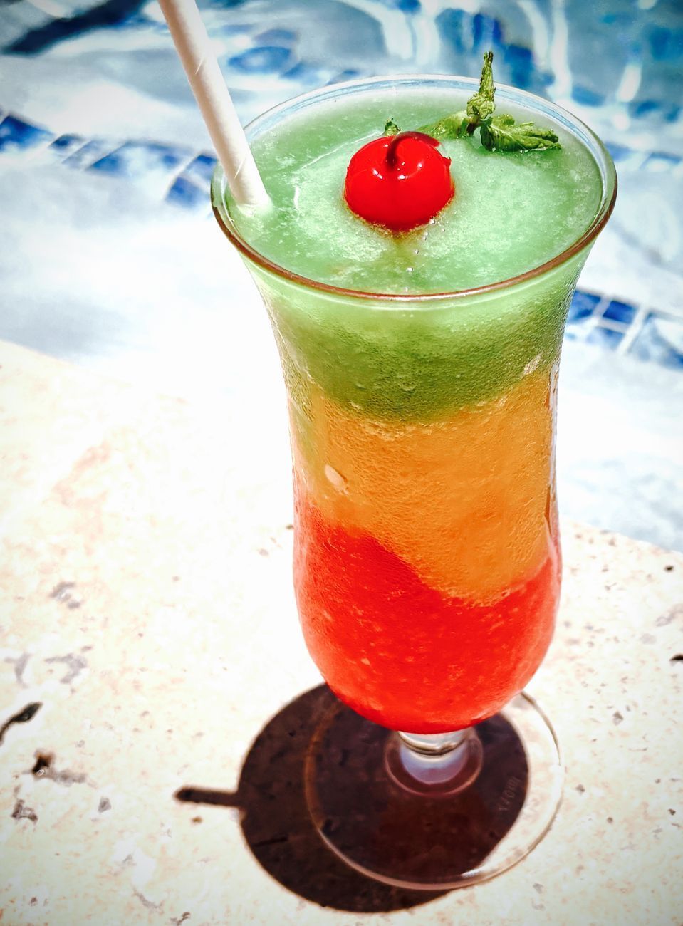 Layered tropical cocktail with cherry and straw.