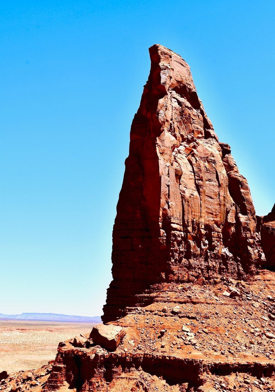 Red sandstone spire against a blue sky, in a desert landscape.