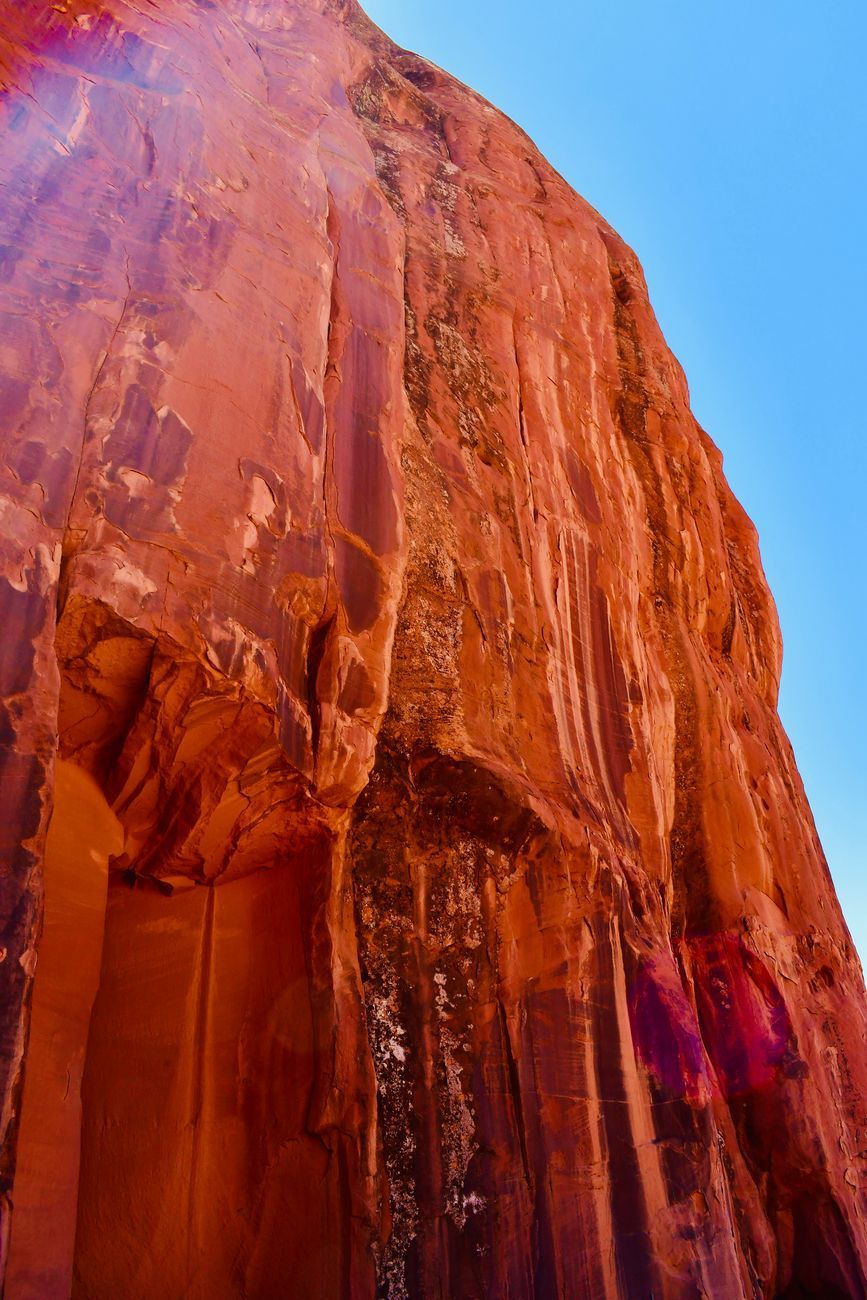 Red sandstone cliff against a blue sky. Vertical lines and textures dominate the weathered rock face.