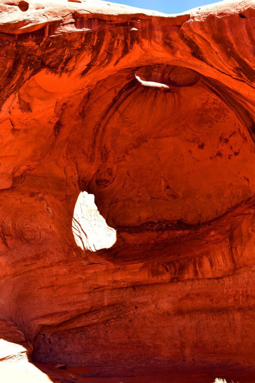 Red rock formation with two openings, lit by sunlight.