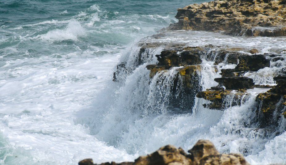 Waves crashing against rocky coastline, forming white foam and spray.