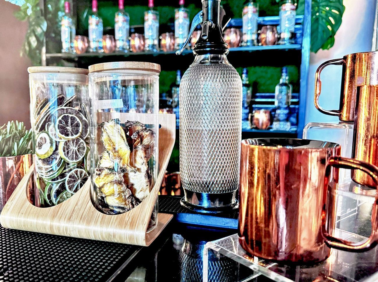 Bar setup with copper mugs, glass jars of dried citrus, and bottles on shelves.