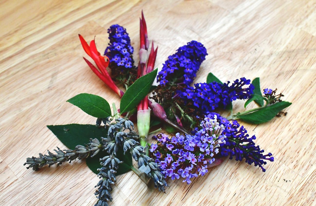 Purple and red flowers, green leaves on wooden surface.