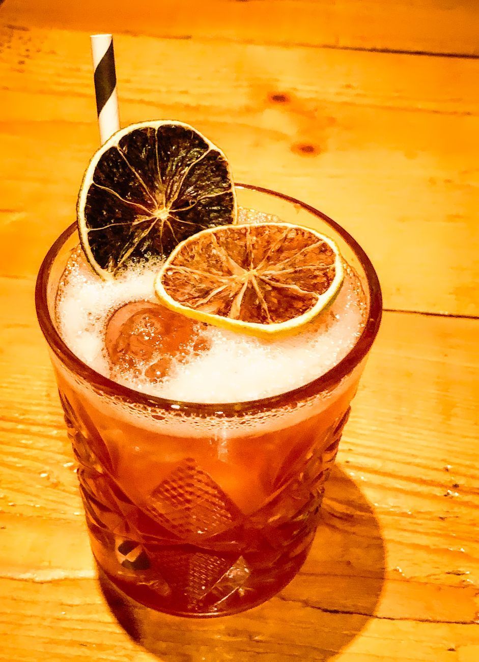 Cocktail in a patterned glass, garnished with dried citrus and a striped straw, on a wooden surface.