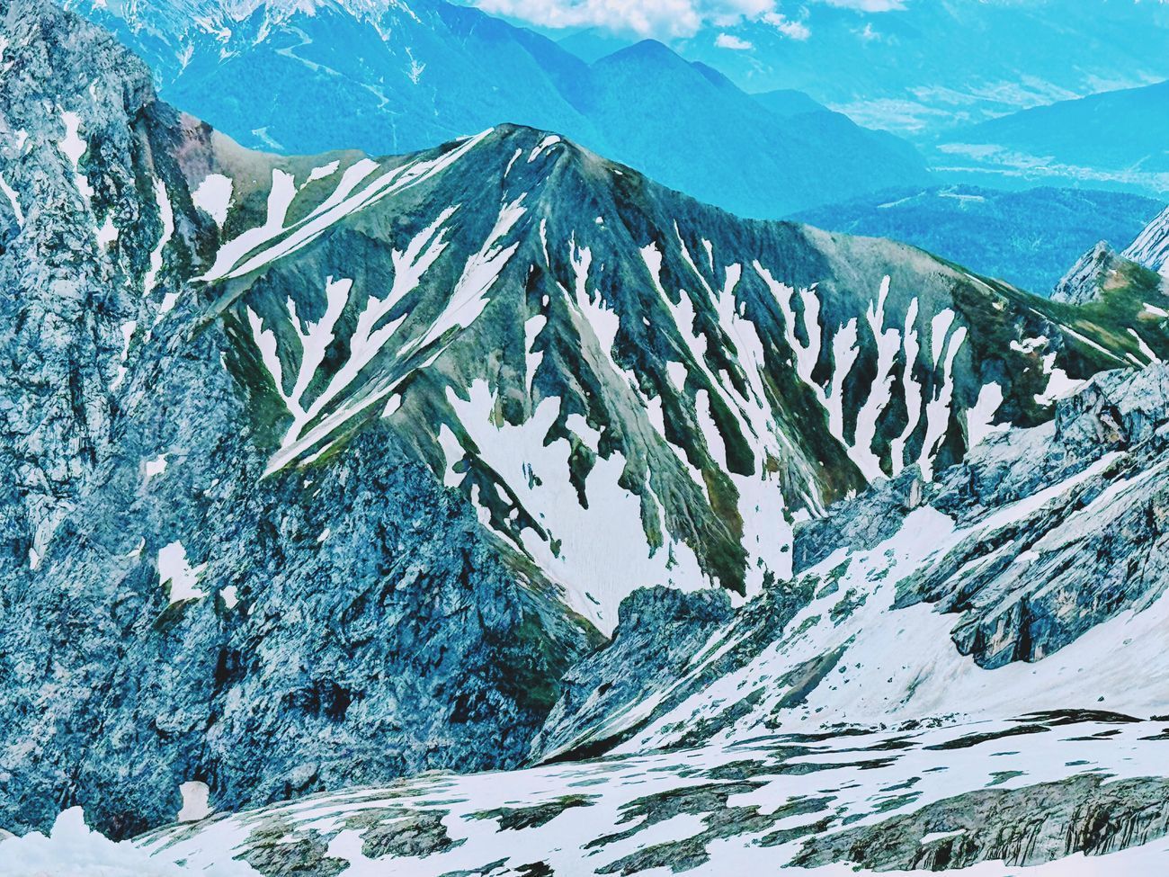 Snow-covered mountain range with patches of green, under a blue sky.