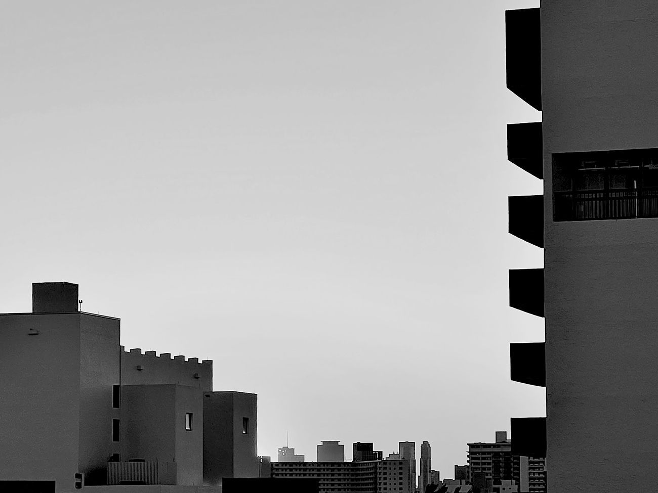 Black and white cityscape with rectangular buildings and open sky in the middle distance.