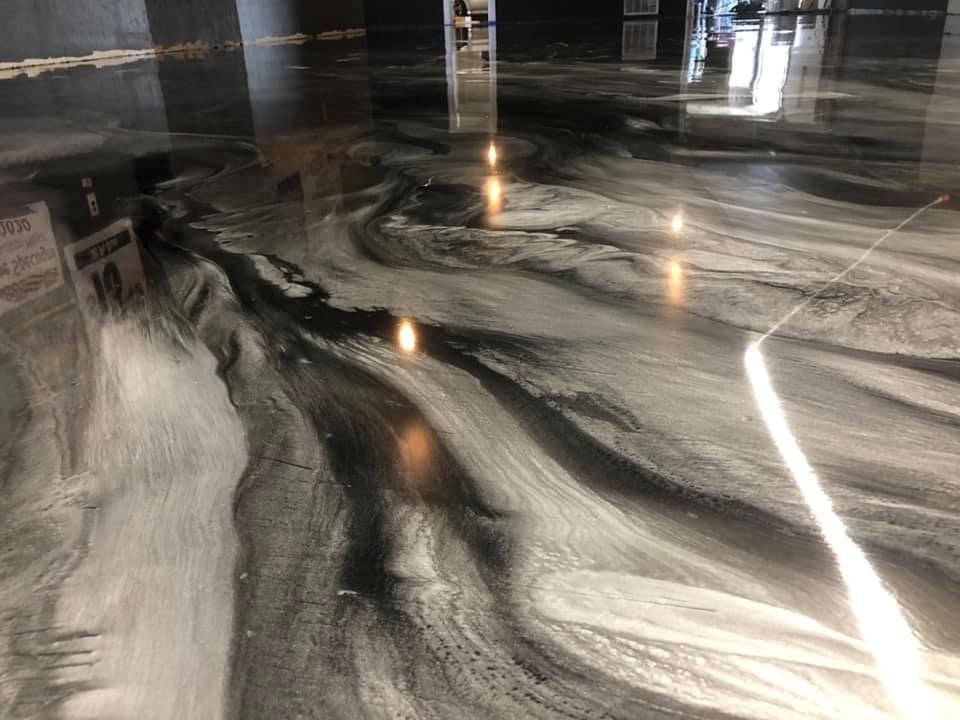 A high-gloss epoxy floor featuring a marbled, swirling pattern of metallic silver and deep black tones.