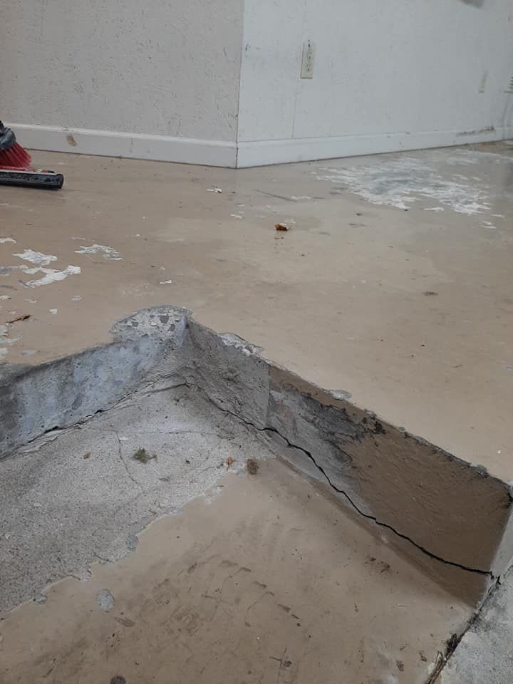 A cracked concrete floor transition in an indoor setting, showing a raised section and exposed rough material.