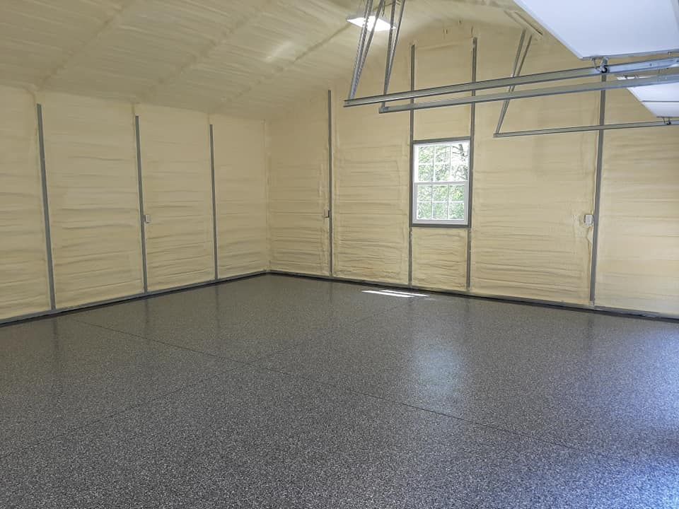 An empty garage with a grey speckled epoxy floor, insulated beige walls, a small window, and overhead door tracks.