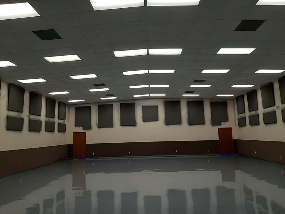 Empty multipurpose room with a glossy gray floor, beige walls, brown wainscoting, and acoustic panels near the ceiling.