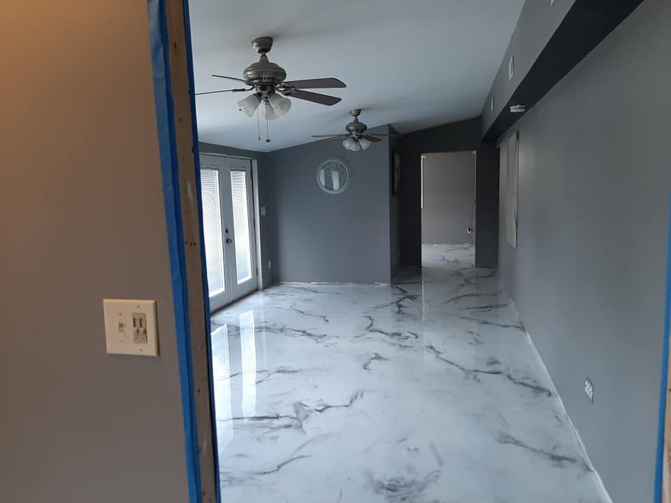 An indoor space with a high-gloss, white-and-gray marble-patterned floor, gray walls, and two ceiling fans.