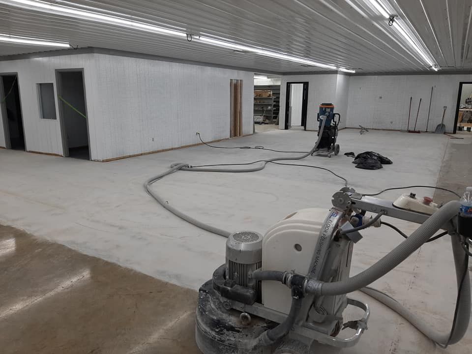 Floor grinding machine on a concrete floor in a room under construction with white walls and overhead lights.