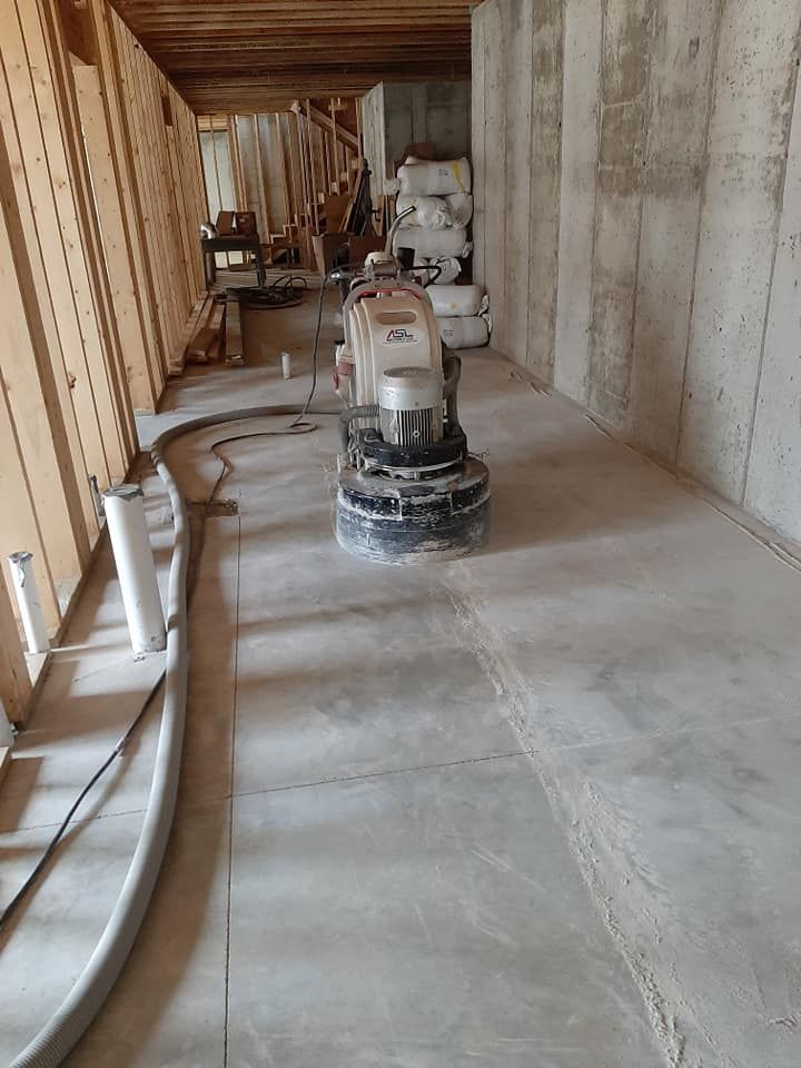 A concrete floor grinding machine sits in a construction space with framed walls and a poured concrete foundation.