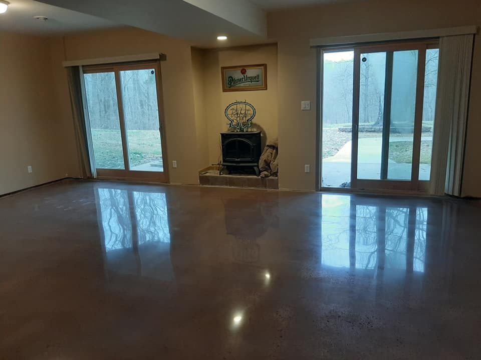 A living room with a polished concrete floor, a central wood-burning stove, and two sliding glass doors to the outdoors.