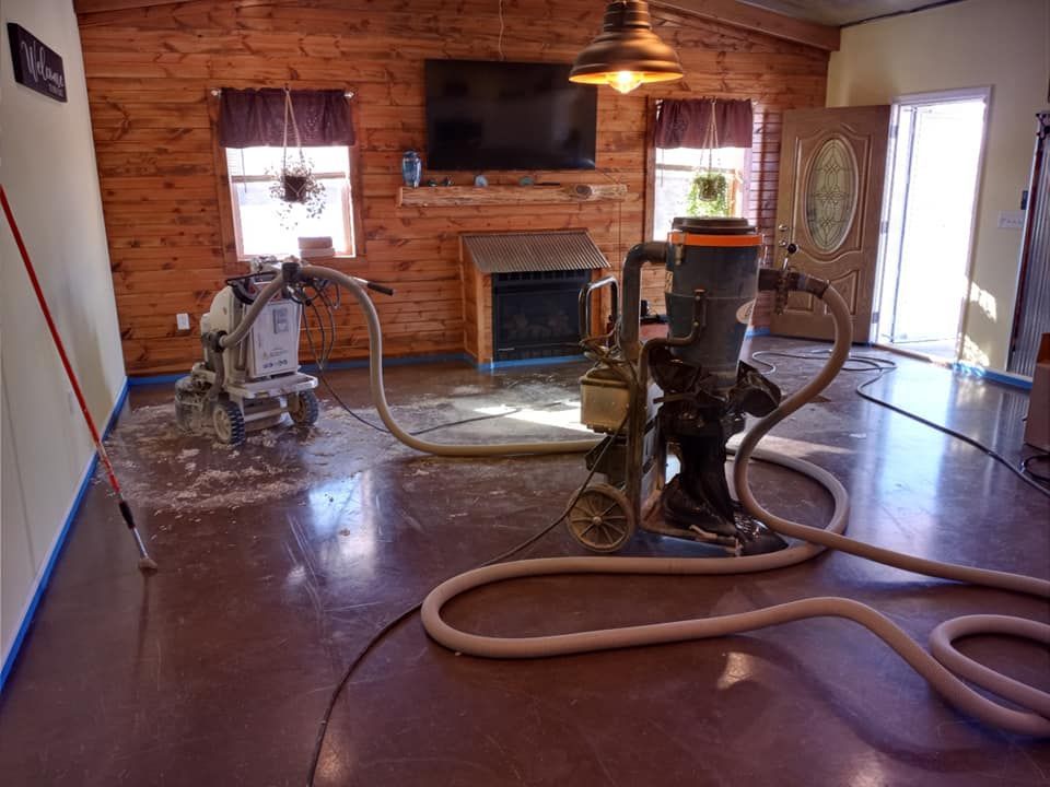 A floor sander and industrial vacuum connected by a long hose in a room with wood-paneled walls and a fireplace.