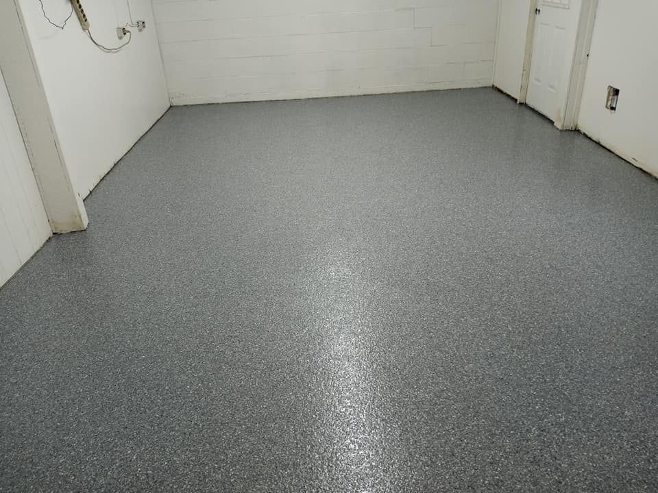 A clean, grey garage floor with a decorative speckled epoxy coating between white concrete block walls.