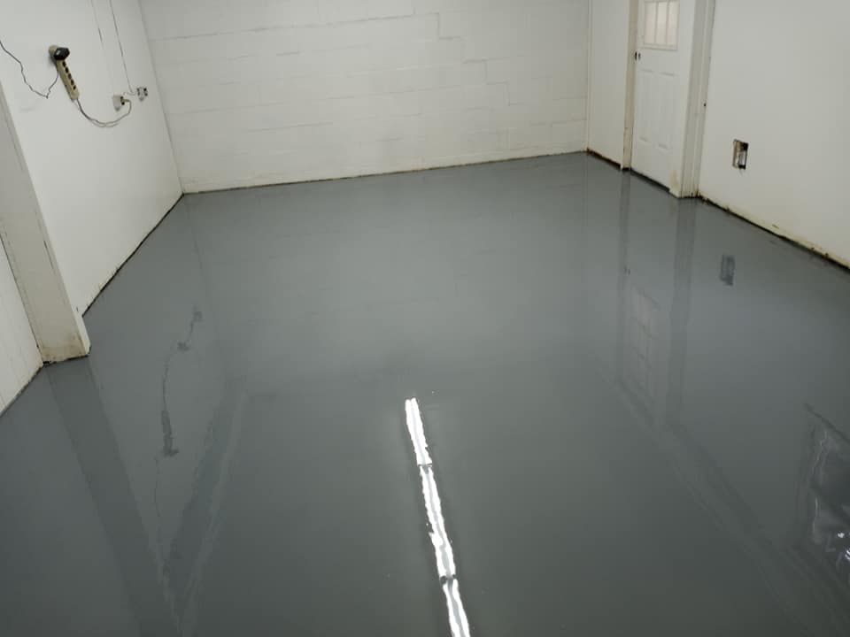 A room with a smooth, glossy, gray epoxy-coated floor reflecting the overhead lighting against white block walls.