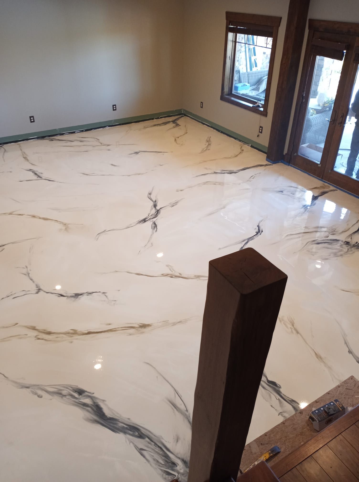 A high-gloss white epoxy floor with gray and black marble-like veining in a room with wood accents and a large door.